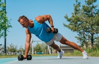 Muscular man performing a dumbbell renegade row plank exercise outdoors for core and strength training.