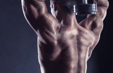 Muscular man performing overhead tricep extensions with a heavy dumbbell to build back and arm muscles.