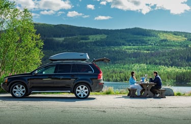 Scenic travel photograph of a couple having a picnic lunch by a lake, backed by forested mountains.