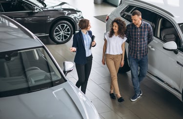 A female car saleswoman talks to a couple, walking through a car showroom.