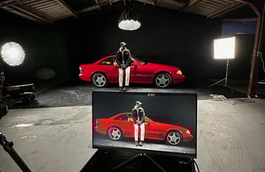 homme dans un studio video sur fond noir avec une voiture mercedes rouge éclairée par des lumières