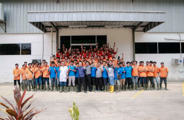 A large group of industrial warehouse employees in orange and blue uniforms posing outside a factory building.