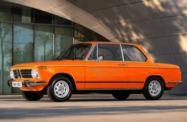BMW 1602e de 1972 exposto diante de arquitetura moderna em imagem histórica
