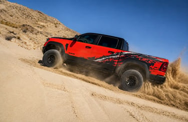 Picape Ram TRX vermelha acelerando em duna no deserto com areia levantando
