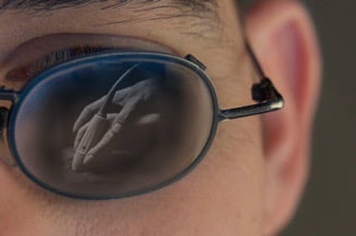 Eyeglasses showing reflection of trainer's and student's hands on an ultrasound probe.
