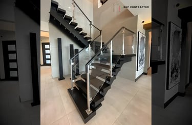 Modern floating staircase with black wood steps and a sleek glass railing system in a luxury home.