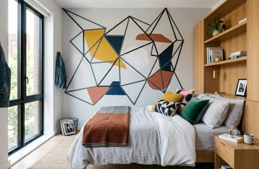 Modern bedroom featuring a geometric wall mural, wooden headboard with shelving, and colorful throw pillows.