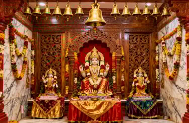 Ornate Hindu temple interior featuring golden deity statues, floral garlands, and hanging brass bells.