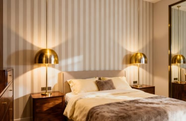Modern bedroom with gold dome pendant lights, striped wallpaper, and a cozy bed with plush pillows.