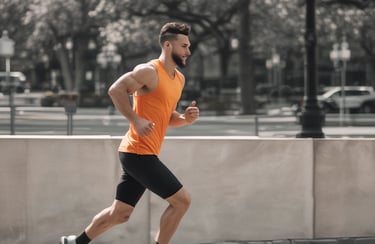 Athletic man in an orange tank top and black shorts jogging on a city path for morning exercise.