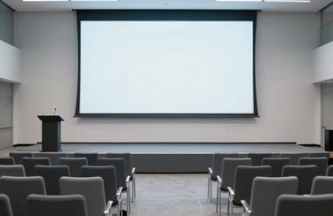 Clean photography of a modern event hall in Minneapolis. A minimalist stage is set with a podium and a large blank projection screen. The seating is arranged for a tech talk, with sleek contemporary chairs. Lighting is crisp and cool, utilizing a light gray and slate blue color scheme. North American / US.