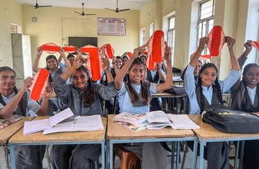 Class of young schoolgirls holding up a Hanaru reusable sanitary napkin in a schoolroom