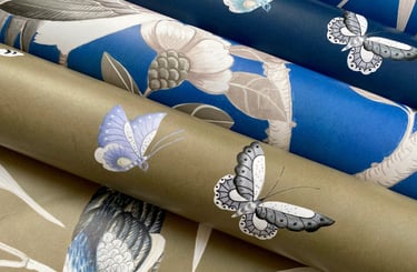 Rolls of luxury designer wallpaper featuring bird and butterfly motifs in blue and gold colors.