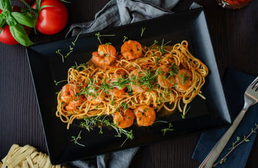 Italienische Pasta mit gebratenen Garnelen, Tomatensauce und frischer Kresse auf schwarzem Teller.