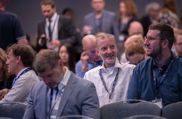 A smiling professional man sitting in a crowded conference room during a business seminar.