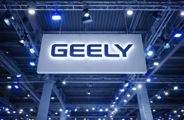 Logo da Geely iluminado em ambiente industrial com estrutura metálica e luzes azuis