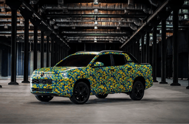 Nova picape VW Tukan camuflada exibida em galpão industrial com iluminação dramática.