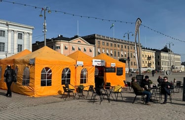 a group of people sitting around tables outside orange tents