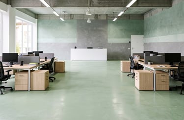 Modern open-plan office with industrial concrete ceilings, green floors and ergonomic workstations.