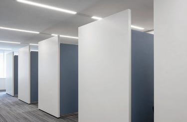 Professional photography of a contemporary office interior in Madrid. Focus on sleek plasterboard partitions and modern ceiling design. The space is bright, professional, and corporate, featuring a palette of white and slate blue grey.