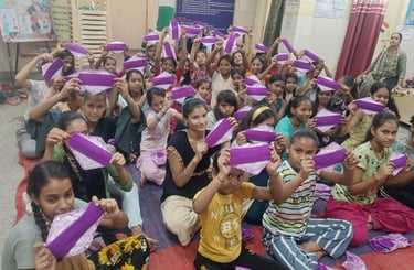 Group of about forty girls sitting on the floor holding up fabric sanitary napkins.