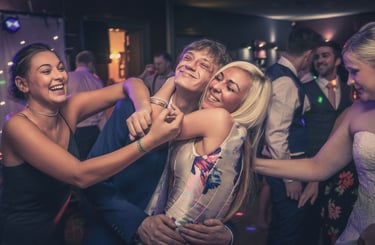 Friends laughing and hugging on a dance floor at a wedding reception party with club lighting.