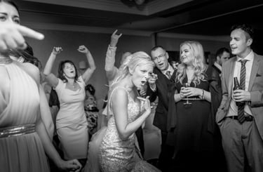 A joyful bride dancing with wedding guests during a black and white reception celebration.