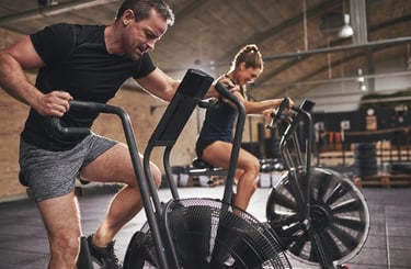 Man and woman performing high-intensity interval training on air bikes at a modern gym.