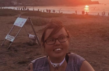 Photo of Stacey at the beach at sunset, smiling big with her hair blown by the wind. 