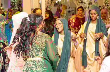 Somalian bride dancing with happy bridesmaid, both in traditional gold & green dresses 