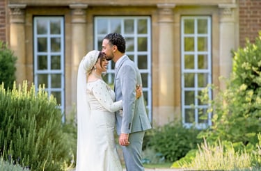asian bride and groom outside stately home, groom kissing bride, brushes are framing the couple 