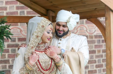 asian bride and groom, both in traditional gold and cream outfits, bride looking to side and groom looking at bride smiling  
