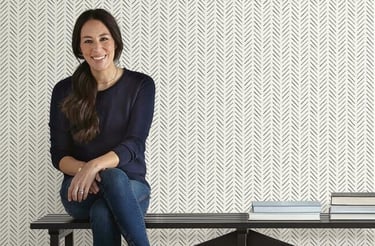 Joanna Gaines sits on a black bench against black and white herringbone peel and stick wallpaper.