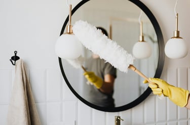 Cleaning a mirror with care — a gloved hand holding a duster in a bright, clean bathroom