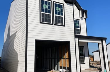 New modern two-story house construction with white lap siding and black window trim.