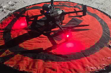 Professional quadcopter drone on a red landing pad at night in a snowy field with glowing red LED lights.