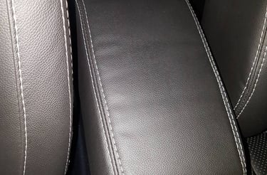 Revestimento de apoio de braço central automotivo em material escuro com costura dupla branca.