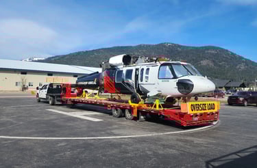 a helicopter being hauled on a long red trailer behind a truck