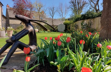 Bronze hare sculpture in a sunny garden with blooming orange tulips and a green lawn.