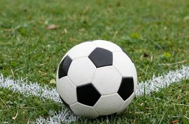A close-up of a football on lush green grass under stadium lights at dusk.