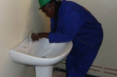 Plombière en combinaison bleu installant un lavabo sur colonne dans une entreprise de Yaoundé