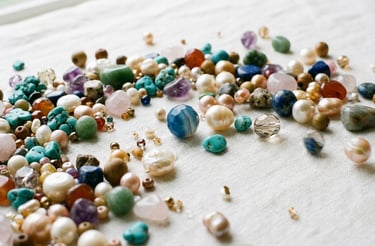A variety of colorful loose gemstone beads and pearls scattered on a white fabric background.