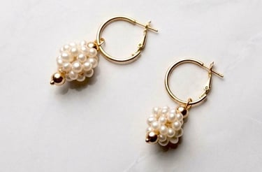 Elegant gold hoop earrings featuring a cluster pearl drop charm on a white marble background.