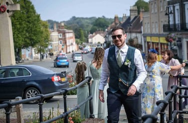 A smiling groom in a plaid waistcoat walking towards Bury St Edmunds Registry Office