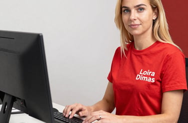 A professional woman smiling while typing on a laptop in a modern office setting.
