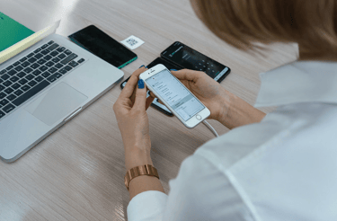 Woman at desk in Cedar Rapids setting up iPhone with other phones, laptop, and QR code for tech help.