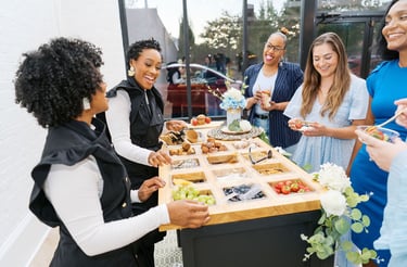 a group of people standing around a table with food