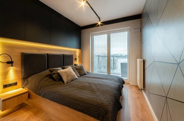 Nowoczesna sypialnia z łóżkiem, ciemnym zagłówkiem, drewnianą podłogą i oknem z żaluzjami