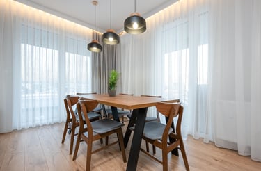 Drewniany stół z sześcioma krzesłami w jasnej jadalni z dużymi oknami i lampami