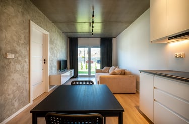 Salon z aneksem kuchennym: stół, sofa, telewizor oraz drzwi balkonowe.